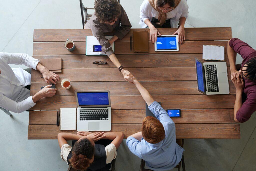 Two businesspeople shake hands as others sit around a table.
